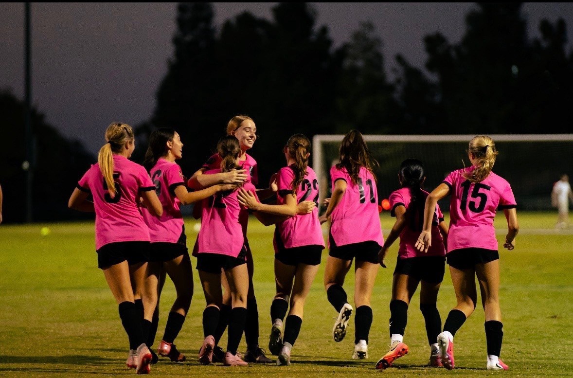 The Lady Pumas in pink uniforms celebrating on the field